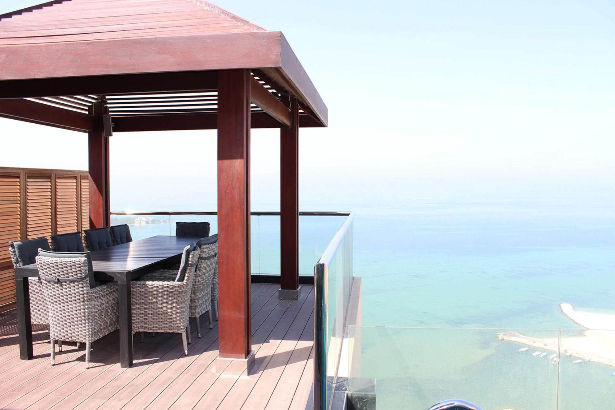 라구나 비치 럭셔리 리조트 앤 스파 마나마 외부 사진 The photo showcases a stylish outdoor patio or terrace area. It features a wooden structure with a sloped roof, providing a shaded space. There is a large table made of dark wood, surrounded by several wicker chairs. The patio is elevated and has gla