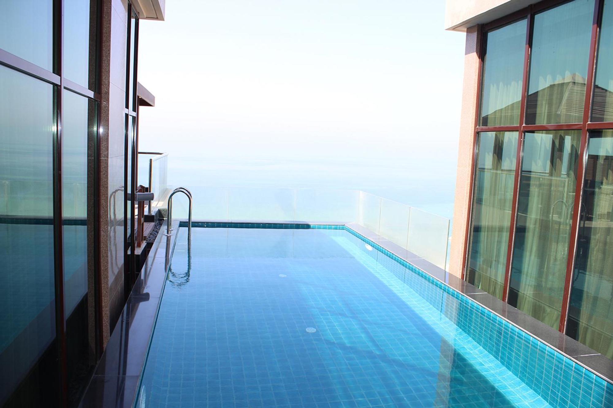 라구나 비치 럭셔리 리조트 앤 스파 마나마 외부 사진 The photo shows an infinity pool situated on a balcony or rooftop, with a clear view extending to the horizon. The pool has a sleek design with blue tiles, and it appears to be reflecting the sky. There is a ladder on one side for access into the poo