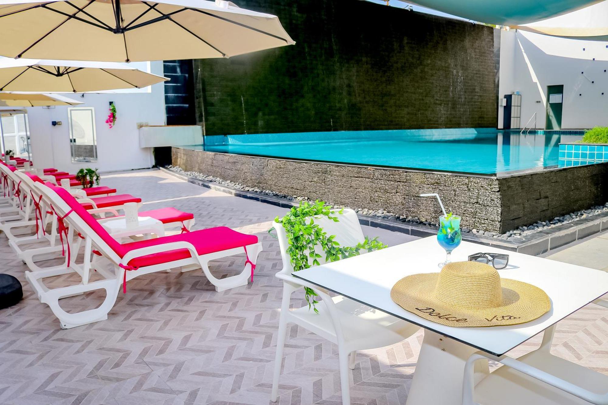 라구나 비치 럭셔리 리조트 앤 스파 마나마 외부 사진 The photo shows a sunny poolside area with bright red lounge chairs arranged neatly beside a swimming pool. There are large beige umbrellas providing shade. A small table is set up with a straw hat and a colorful drink, suggesting a relaxed, tropical