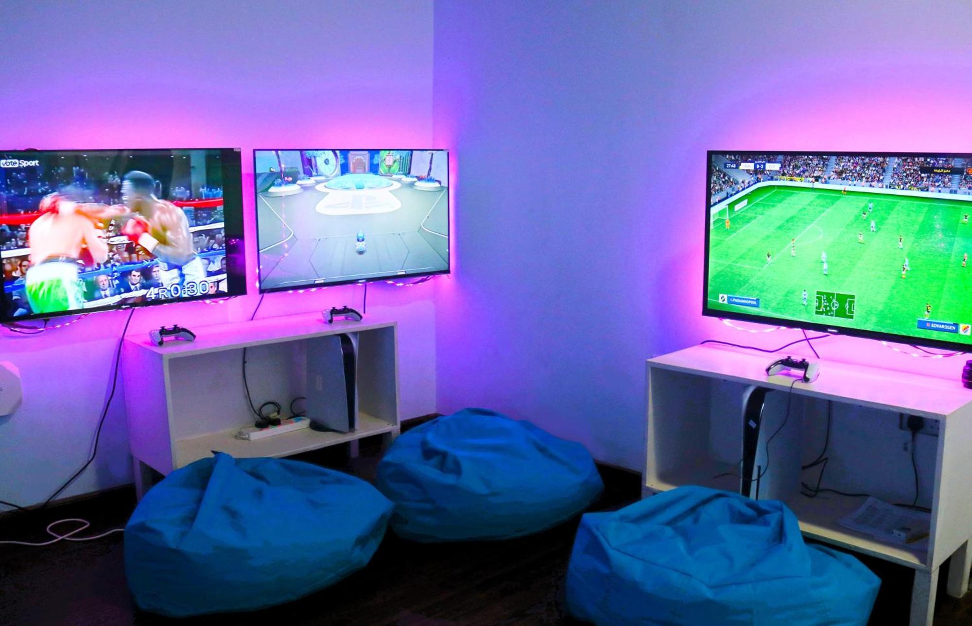라구나 비치 럭셔리 리조트 앤 스파 마나마 외부 사진 The photo shows a gaming area featuring three televisions mounted on the wall, displaying different games. Two of the TVs are showing gaming scenes, with one depicting a boxing game and the other showing a vibrant game environment. The third TV displ