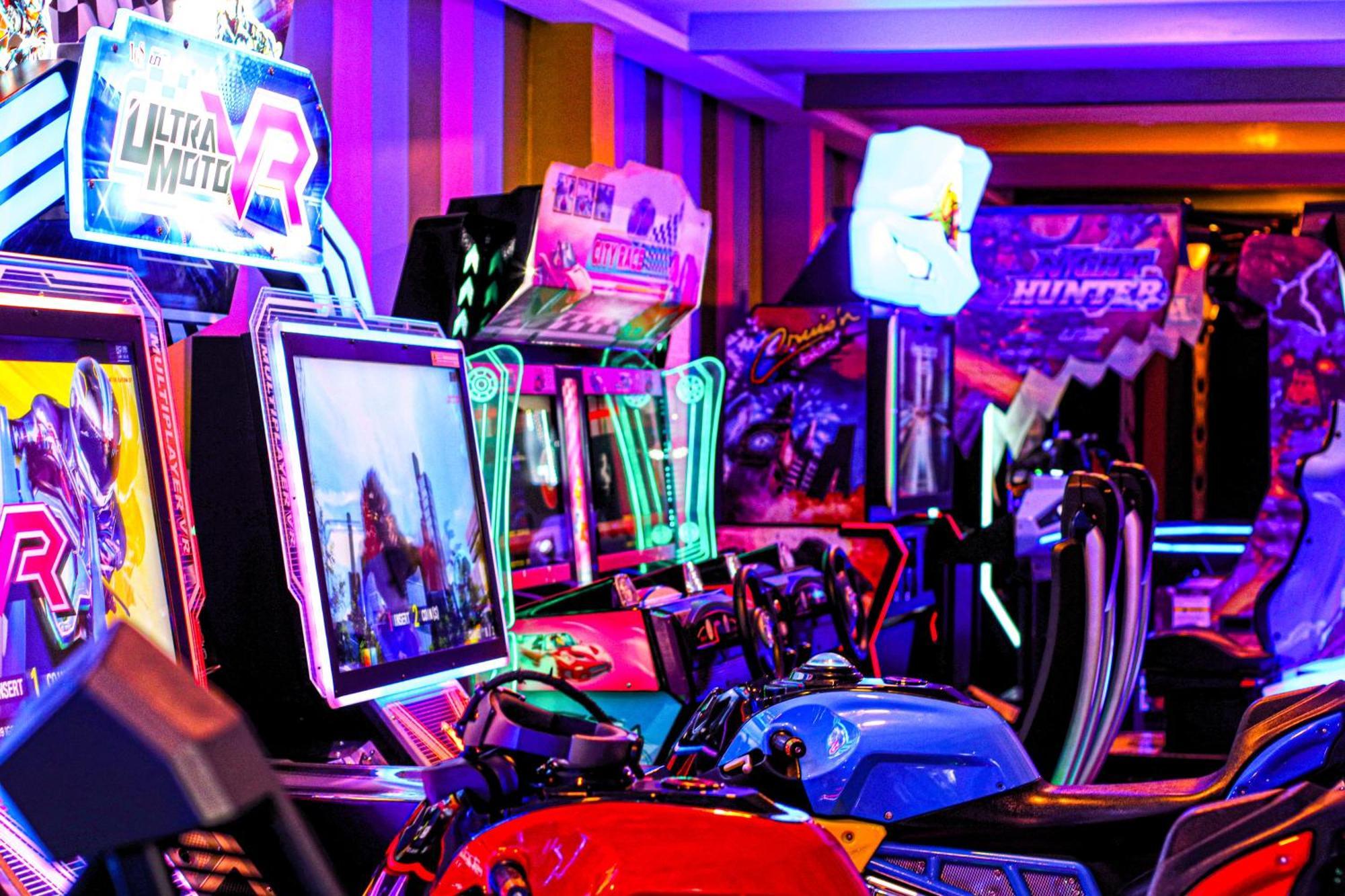 라구나 비치 럭셔리 리조트 앤 스파 마나마 외부 사진 The photo shows a vibrant arcade scene featuring various arcade gaming machines. The machines are lined up, showcasing colorful screens and bright, neon lights, creating an energetic atmosphere. Some machines appear to be racing games, as indicated b