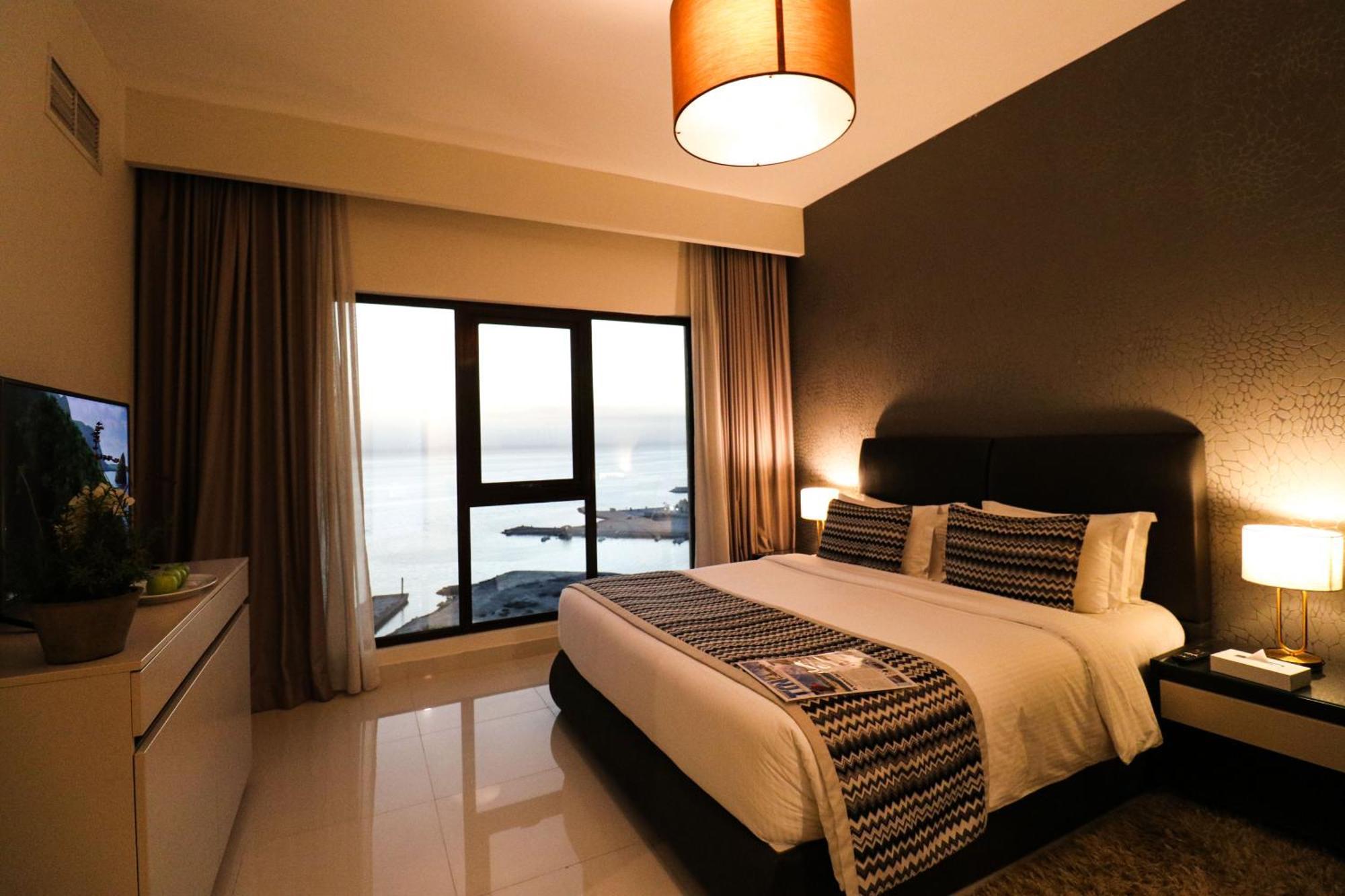라구나 비치 럭셔리 리조트 앤 스파 마나마 외부 사진 The photo shows a modern hotel room featuring a neatly made bed with decorative pillows. The room has a stylish design with a dark accent wall and a large window that offers a view of the outdoors. Natural light comes in, giving the space a bright an