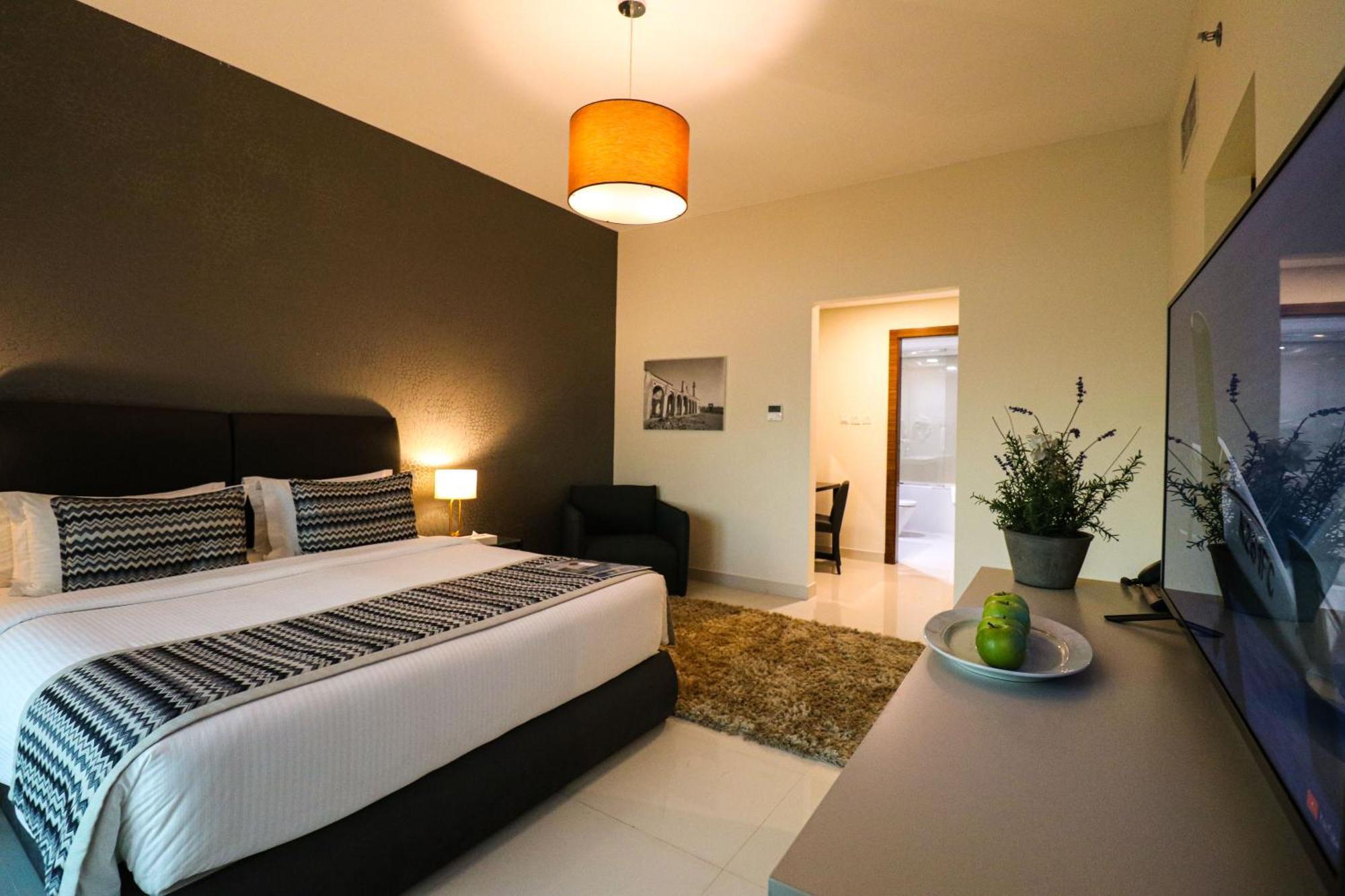 라구나 비치 럭셔리 리조트 앤 스파 마나마 외부 사진 The photo shows a modern hotel room. It features a large bed with a neatly made white and dark-colored duvet. On either side of the bed, there are bedside tables with lamps. The wall behind the bed is painted in a dark color, creating a contrast with
