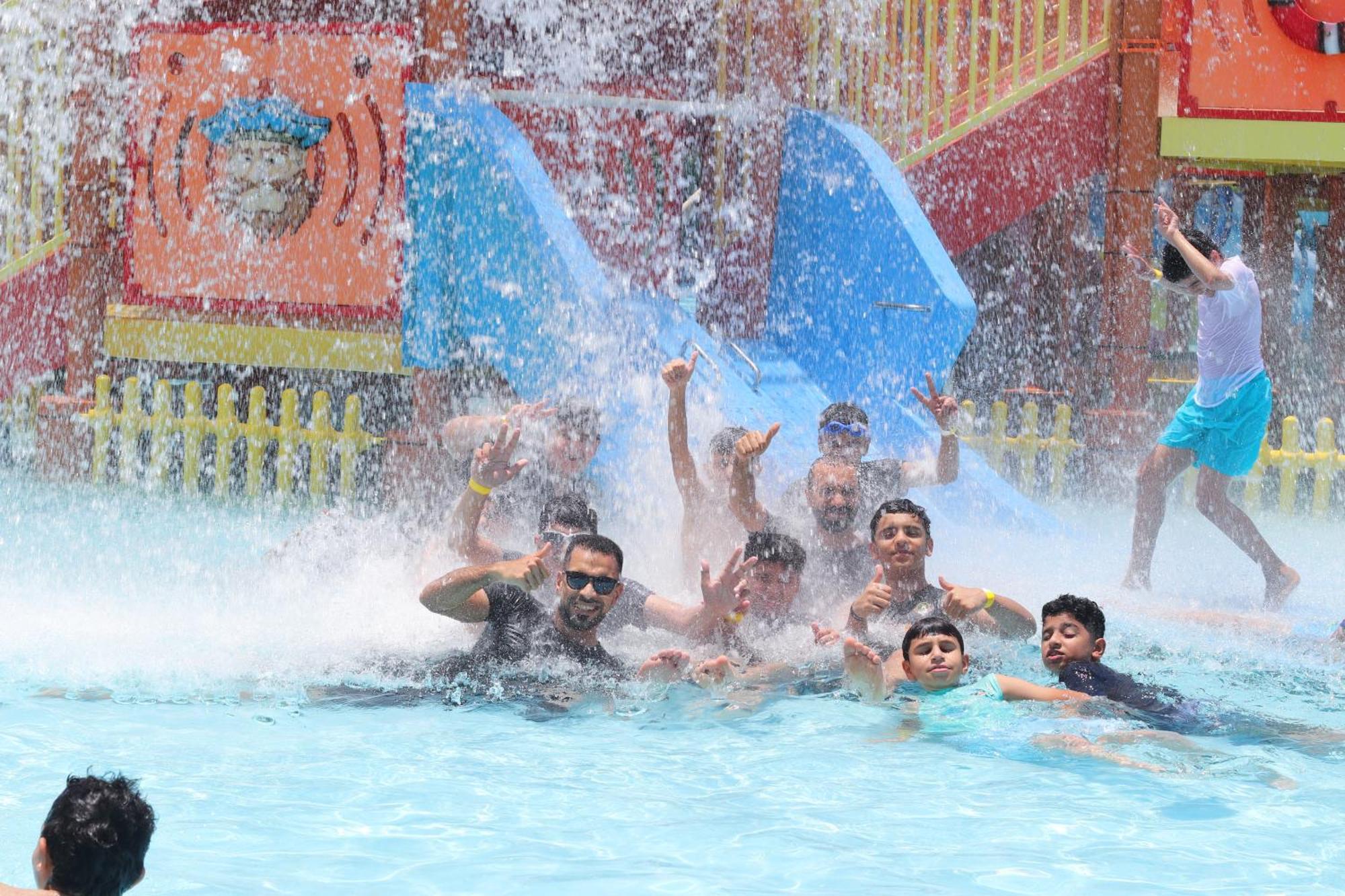 라구나 비치 럭셔리 리조트 앤 스파 마나마 외부 사진 The photo shows a lively scene at a water park or pool area. Several people, including adults and children, are enjoying themselves in the water, splashing and posing for the camera. Water is cascading down, creating a refreshing atmosphere. In the b