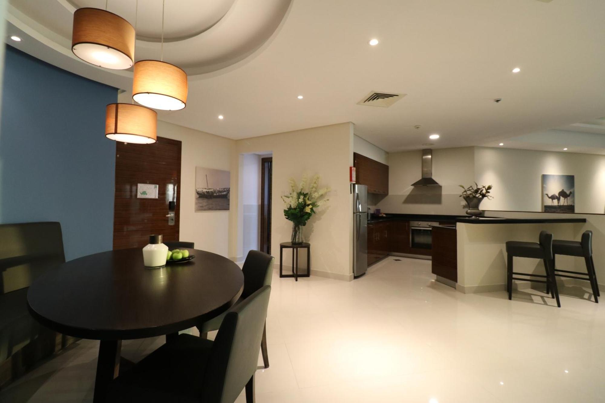 라구나 비치 럭셔리 리조트 앤 스파 마나마 외부 사진 The photo shows a modern, open-concept dining and kitchen area. On the left, there is a round dining table with black chairs, accompanied by a few decorative elements like a small vase and some fruit. The walls have a combination of light and dark to