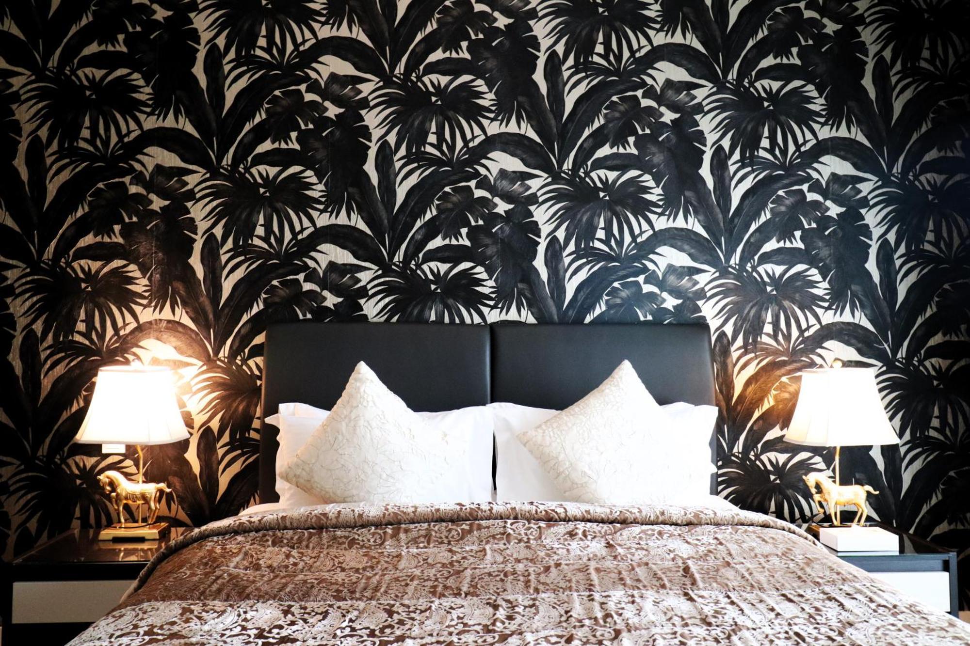 라구나 비치 럭셔리 리조트 앤 스파 마나마 외부 사진 The photo depicts a stylish bedroom featuring a distinctive wall covered in a black and white tropical foliage wallpaper. The bed has a modern black headboard and is adorned with white pillows, creating a clean and elegant look. A textured brown thro