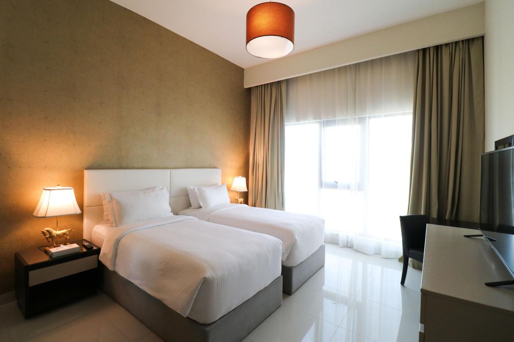 라구나 비치 럭셔리 리조트 앤 스파 마나마 외부 사진 The photo shows a hotel room featuring two single beds with white bedding. The walls have a neutral tone, and there's a large window covered by light, sheer curtains allowing natural light to enter. On either side of the beds, there are bedside table