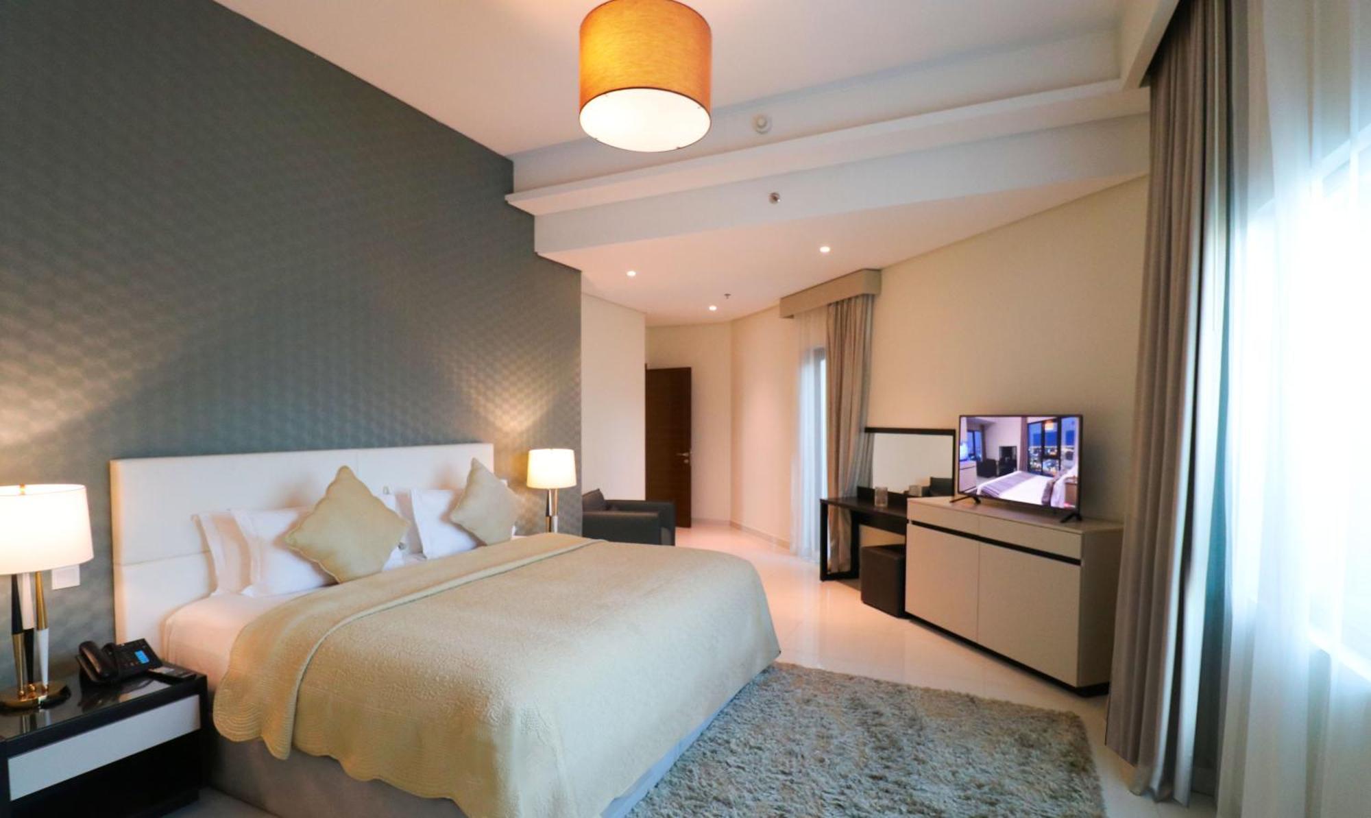 라구나 비치 럭셔리 리조트 앤 스파 마나마 외부 사진 The photo shows a modern hotel room featuring a large bed with a light-colored blanket and decorative pillows. The walls are painted in a subtle shade, and there is a textured accent wall behind the bed. On one side, a bedside lamp provides warm ligh