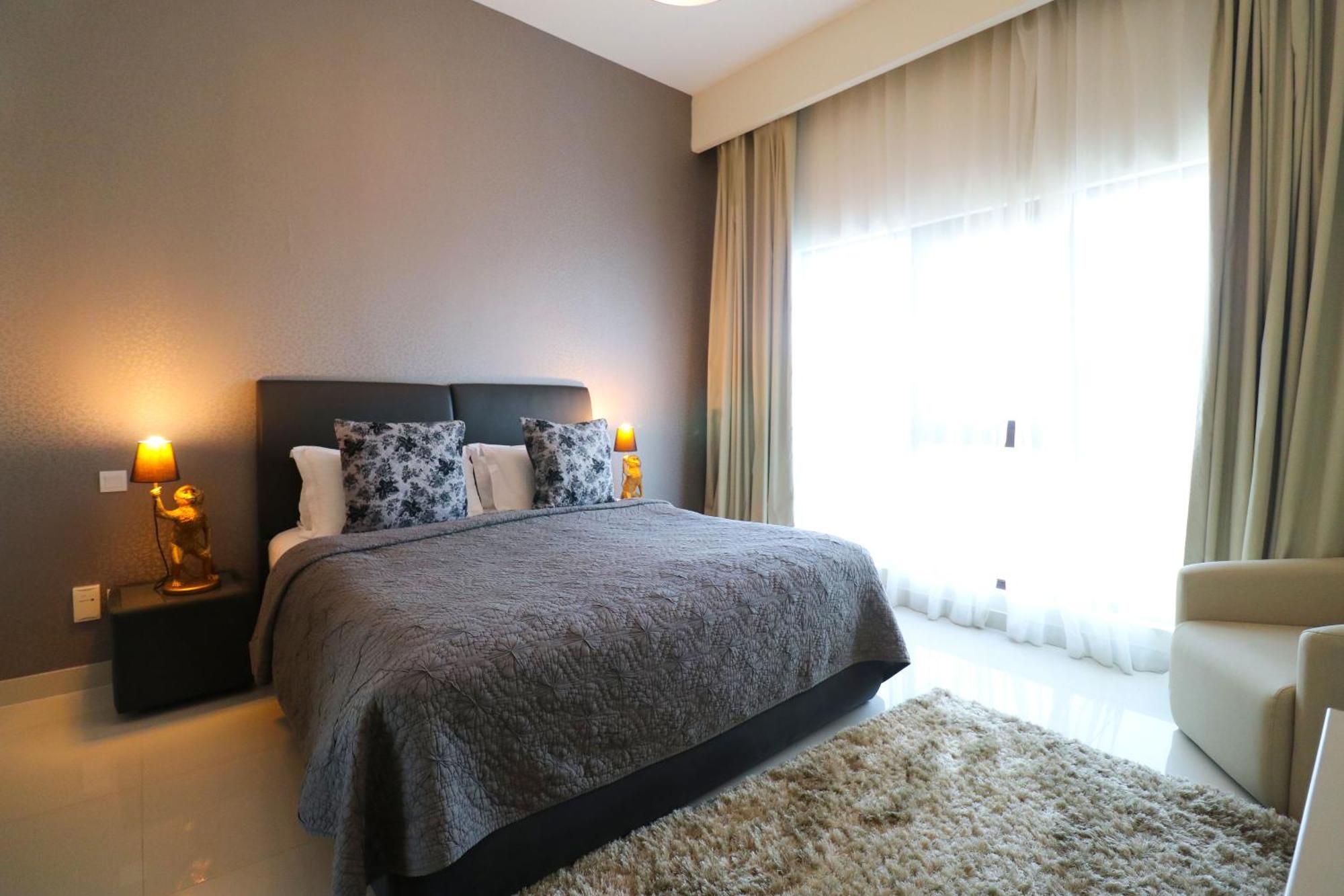 라구나 비치 럭셔리 리조트 앤 스파 마나마 외부 사진 The photo shows a stylish bedroom with a modern design. It features a large bed with a dark gray bedspread and decorative pillows. On either side of the bed are two wooden nightstands, each with a lamp. There is a large window covered with light, flo